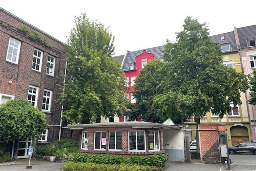 Straßenansicht des Union Gewerbehofs mit Backsteinbau, Bäumen und einem kleinen Flachbau