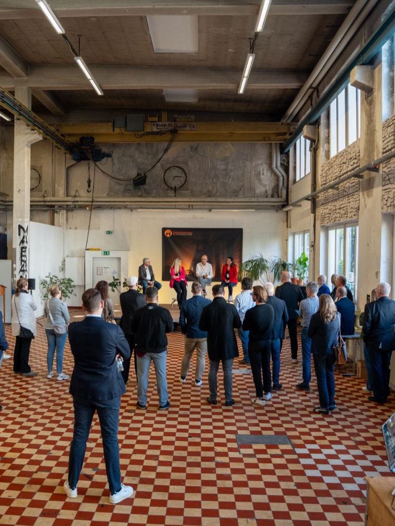 Blick durch die Werkhalle auf die Podiumsdiskussion, davor stehen die Gäste